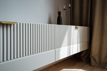 In a cozy living room, there is a white cabinet elegantly placed, adorned with a beautiful vase...