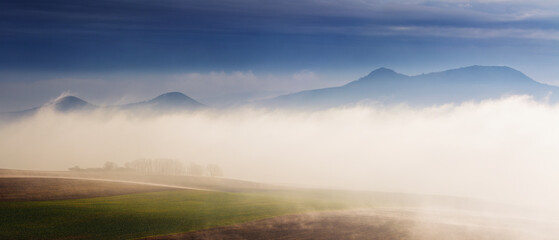 Hills Above Fog Misty Inversion in Warm Sunshine and Dark Clouds