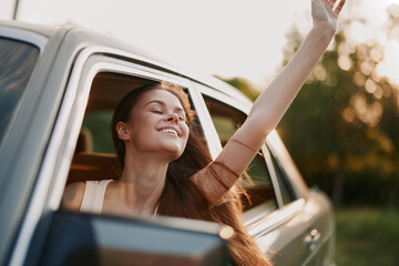 Young woman enjoying freedom with her arm out of the car window on a sunny day, evoking happiness...