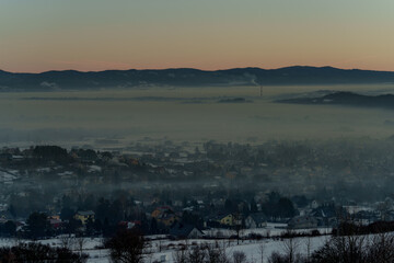 Winter mountain valley with village covered in smog at sunrise