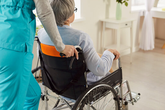 Cropped imaged of handicapped senior woman in wheelchair being assisted by unrecognizable nurse. Supporting caregiver takes care of disabled patient, gives medical help assistance 