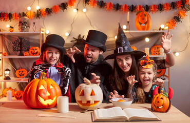 Cheerful family in Halloween costumes making scary faces behind table with glowing carved pumpkins....