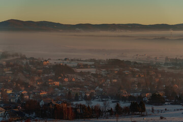 Winter mountain valley with village covered in smog at sunrise