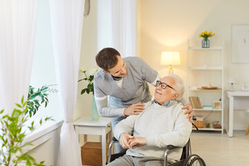 Male nurse providing help to elderly man who is disabled, sitting in wheelchair, giving assistance...