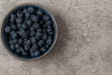 A blue bowl full of tasty blueberries on a concrete background, a healthy snack
