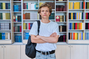 Portrait of handsome confident serious teenage boy looking at camera in library