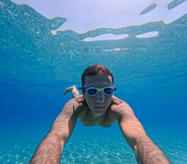 Fototapeta premium Man swimming underwater in the Mediterranean sea off the Sicilian coast. The man is forty years old, of caucasian origin and has swimming goggles on his face