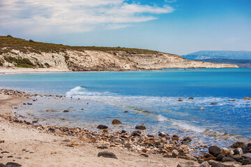 Crystal clear turquoise water gently laps the rocky shore of a secluded beach in Alacati, Cesme, Turkey, creating a tranquil and inviting scene