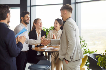 Happy smiling company employees making deal in modern office shaking hands. Business people rejoicing at a successful partnership with a colleagues applauding them on a meeting indoors.