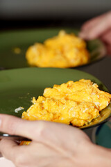 Hands carry scrambled eggs served served on green plates