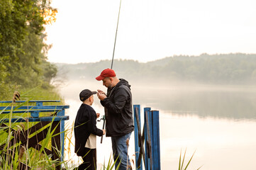 Father helping his son prepare fishing gear on a misty morning by the lake, showing patience and...