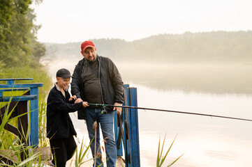 Father teaching his son how to fish on a calm foggy lake, sharing a peaceful and meaningful bonding...