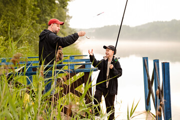 Father and son catch their first fish and laugh together while fishing on a wooden pier by the...