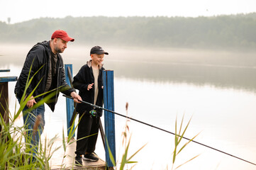 Father teaching his son how to fish on a calm foggy lake, sharing a peaceful and meaningful bonding...