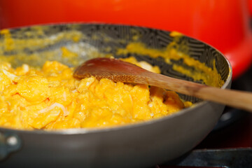 Scrambled eggs being cooked in non-stick frying pan with wooden spoon