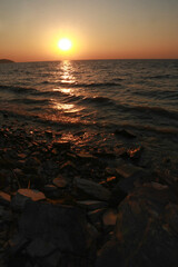 Breathtaking Sunset Over a Serene Ocean with Gentle Waves and Pebbled Shoreline Captured in a...