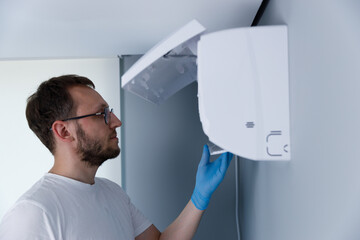 A focused technician wearing blue gloves inspects a white device mounted on a wall, demonstrating...