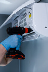 Hand holding a power drill with a bright orange and black design, set against an air conditioning...