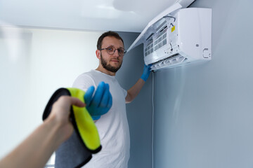 A Professional Male in Protective Gloves Working on an Air Conditioning Unit, Engaged in...