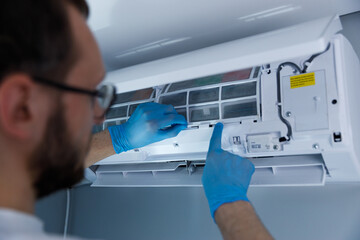 A technician in blue gloves carefully cleans and maintains an air conditioning unit, ensuring...