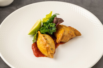 Meat empanadas on tomato sauce, served with fresh greens and lime wedge