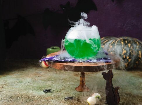 Halloween concept, boiling magical green potion in round glass pot with white smoke on wooden stand