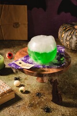 Halloween concept, boiling magical green potion in round glass pot with white smoke on wooden stand