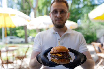 Delicious Gourmet Burger Served by a Person Wearing Black Gloves at an Outdoor Caf Surrounded by...