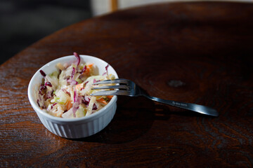 Delicious Coleslaw in a White Dish Accompanied by a Fork on a Wooden Table, Perfect for a Healthy Meal or Side Dish with Vibrant Colors and Fresh Ingredients