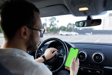 Focused Driving: A Man Navigates His Smartphone While Behind the Wheel in a Modern Car with a Cityscape as His Backdrop, Safety Concerns and Distractions Come to Mind