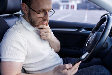 Pensive Young Man in a Car Using Smartphone While Deep in Thought, Reflecting on Something...