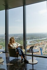 In her stylish and contemporary office, a driven businesswoman takes a welldeserved break, enjoying a steaming cup of coffee while she admires the vibrant cityscape view through her large windows