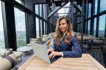 In a modern office with stunning city skyline views, a dedicated businesswoman focuses intently on...