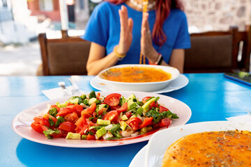 Close up of turkish Tarhana soup seasoned with spices and herbs, next to a fresh salad, enjoyed by a woman in a restaurant