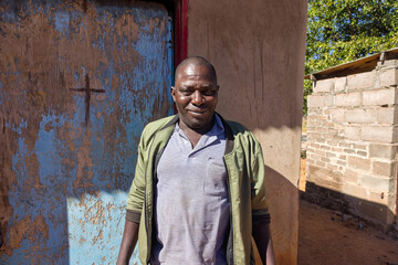 africa village, single african man in the township ,standing outdoors in the yard , in front of his...