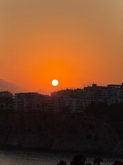 Sunset over Antalya with a rocky coastline and a tourist boat. Warm sky, sea cliffs, and a traditional cruise ship in golden evening light