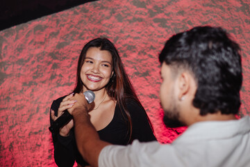 Beautiful young Latina woman with a microphone singing karaoke with a man from the LGBT community