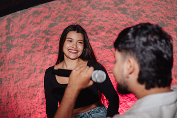 Beautiful young Latina woman with a microphone singing karaoke with a man from the LGBT community