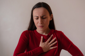 Young woman in red sweater holding her chest with eyes closed, expressing pain or discomfort,...