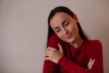 Young woman in a red sweater hugging herself with eyes closed, smiling peacefully, expressing...