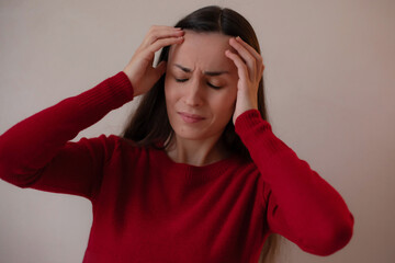Young woman in a red sweater touching her temples with closed eyes, expressing headache, stress, or...