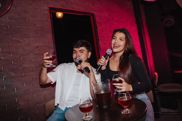 LGBT friends holding a microphone singing in a bar or cafe sitting at a table with beer