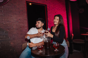LGBT friends holding a microphone singing in a bar or cafe sitting at a table with beer