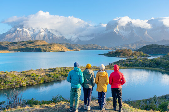 Hikers admire Torres del Paine mountains in Patagonia, Chile. Scenic view with lake, snow-capped peaks, and vibrant outdoor clothing. - Powered by Adobe