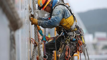 Construction worker expertly securing ropes while wearing safety gear, demonstrating focus and precision. Industrial setting highlights the importance of safety and expertise in high risk jobs