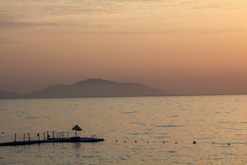 Early morning over the Red Sea. The water surface is covered with smoke and the orange color of the sunrise. In the foreground is a plastic yacht marina. Winter sea beach pier rocks