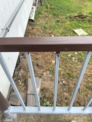 Close up view of a wooden railing on a residential property with a grassy area and debris nearby