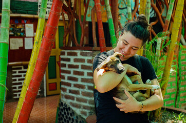 A young woman joyfully embraces a cute puppy outdoors beside colorful bamboo.The vivid and playful background exudes a cheerful atmosphere, making this heartwarming scene lively and full of positivity