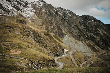 Serpentine mountain road winds through stunning alpine landscape. Dramatic scenery with snow-capped...