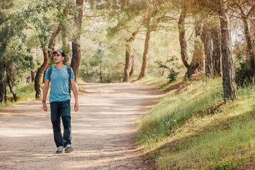 Young male hiker with backpack walking in forest on sunny day enjoying nature and healthy lifestyle